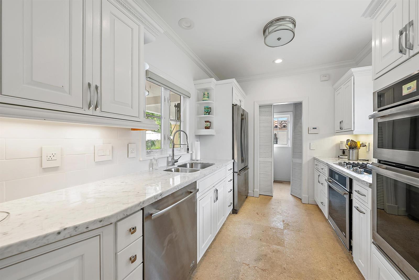 A white kitchen features marble countertops, stainless steel appliances, and light-colored stone flooring — 325 Seaspray Avenue, Palm Beach FL 33480, PALM BEACH, FL