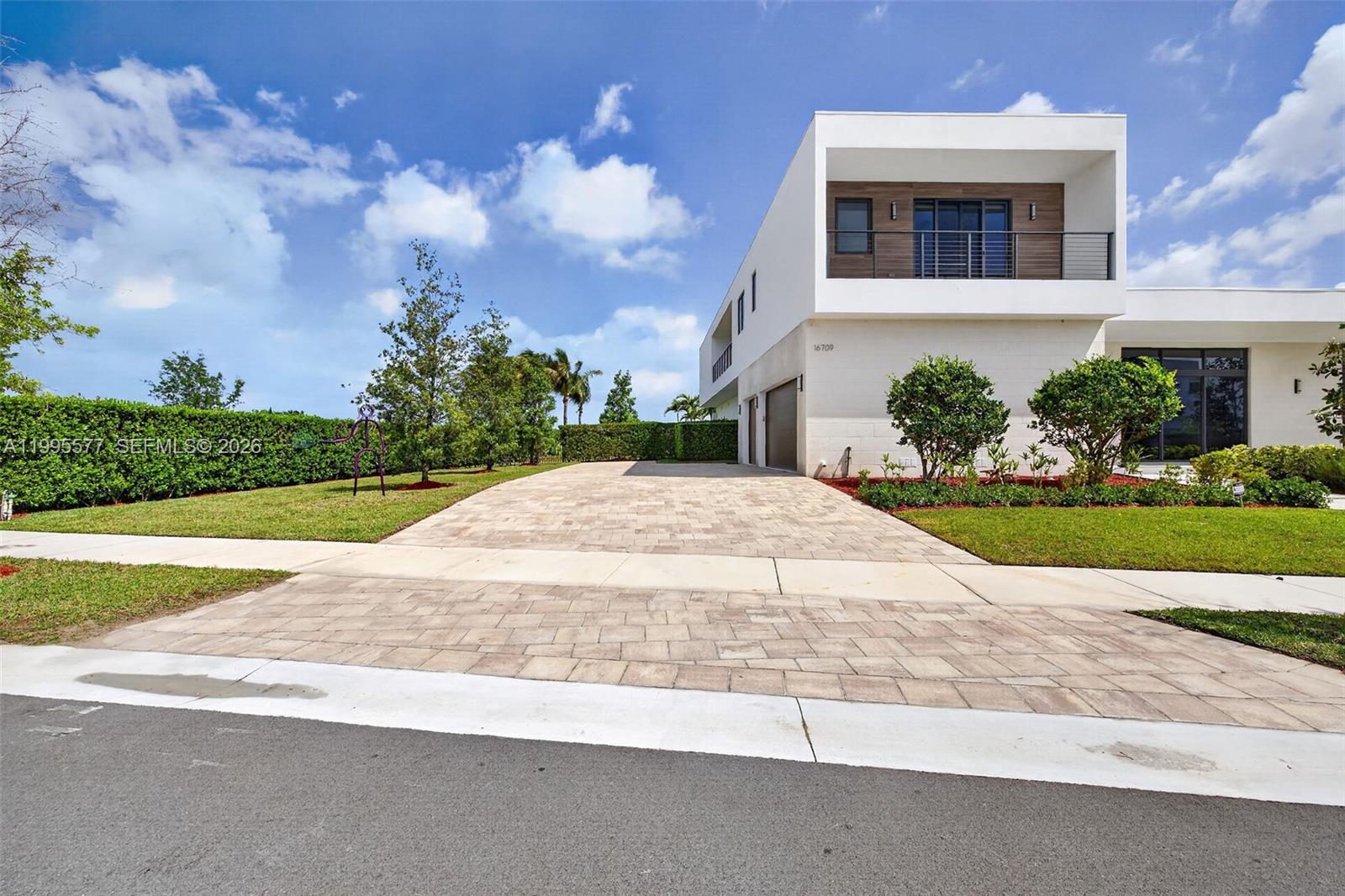 A modern two-story house features a paved driveway, a balcony, and a manicured lawn — 16709 Botaniko Drive North, Weston FL 33326, WESTON, FL