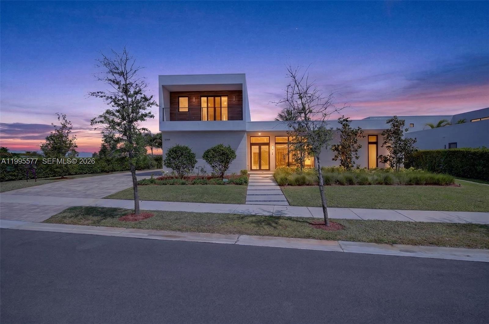 A modern two-story house with a flat roof and wood accents stands at dusk — 16709 Botaniko Drive North, Weston FL 33326, WESTON, FL