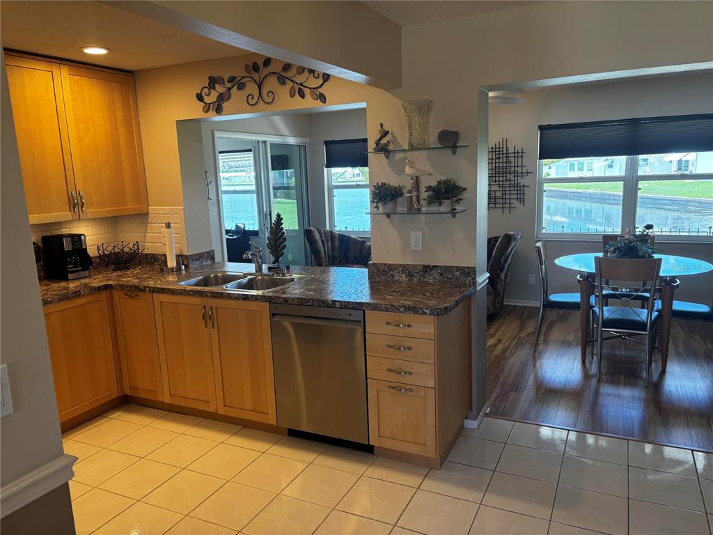 A kitchen with light wood cabinets, granite countertops, and tile flooring overlooks a dining area — 4172 100TH AVENUE N, PINELLAS PARK, FL
