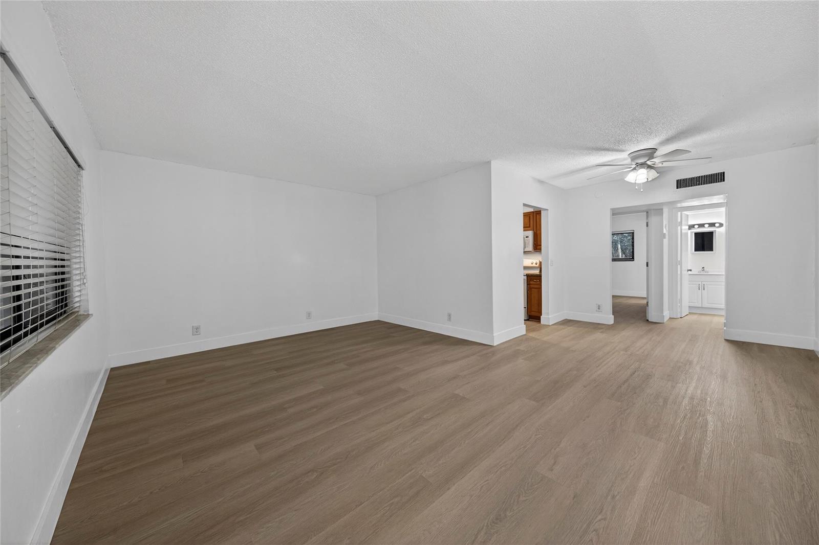 An empty living room features white walls, light wood-look flooring, and a ceiling fan — 2201 NE 36th Street # 105, Lighthouse Point FL 33064, LIGHTHOUSE POINT, FL