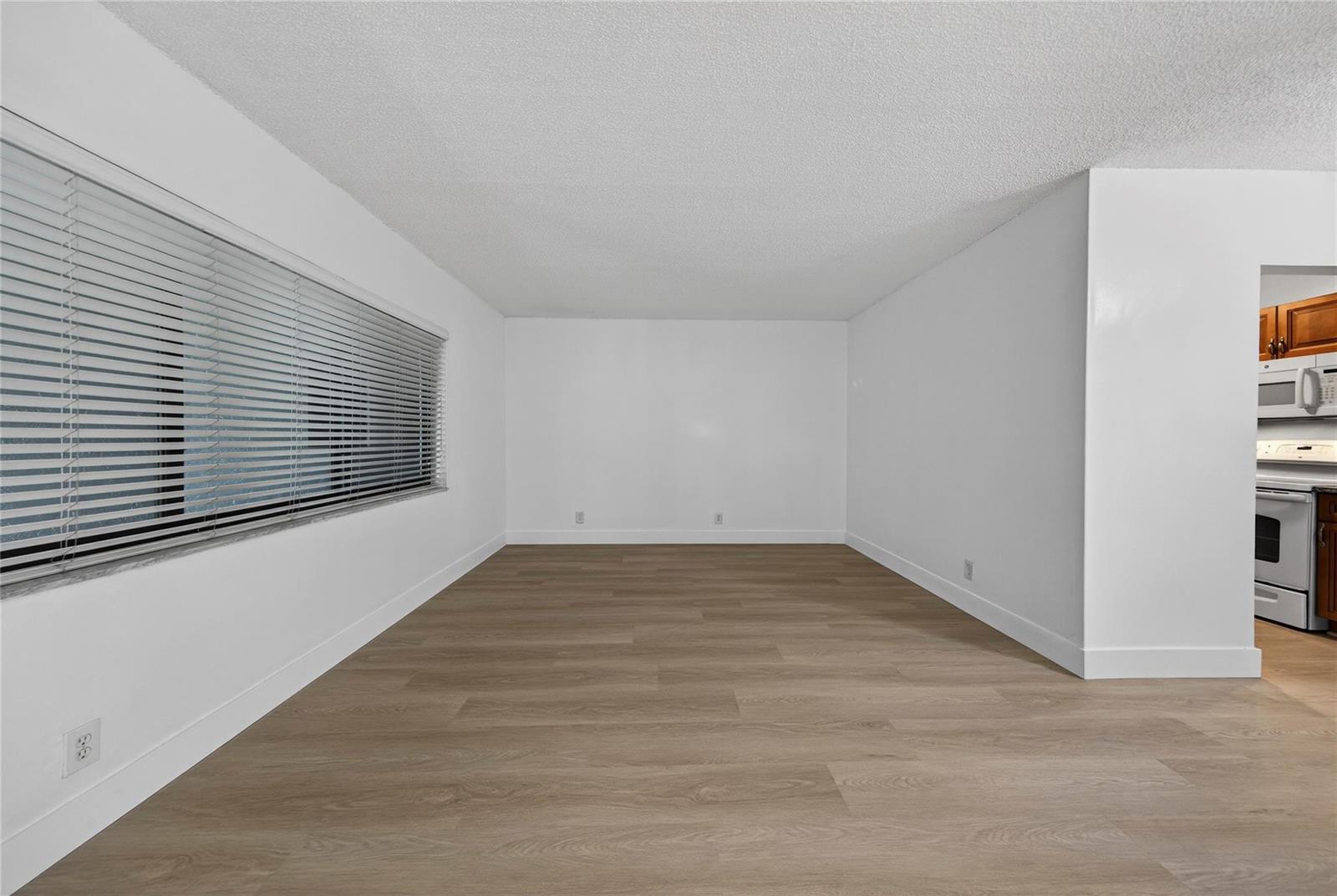 An empty room features light wood-look flooring, white walls, and a large window with blinds — 2201 NE 36th Street # 105, Lighthouse Point FL 33064, LIGHTHOUSE POINT, FL