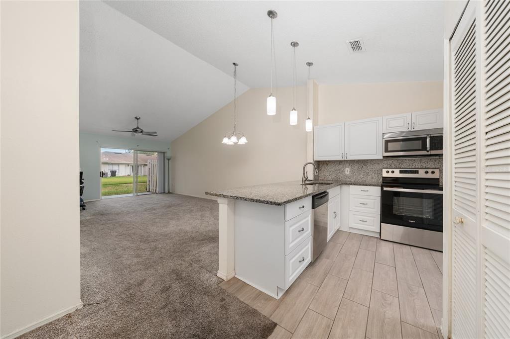A kitchen with white cabinets and granite countertops opens into a carpeted living area — 1262 LUCAYA CIRCLE, ORLANDO, FL