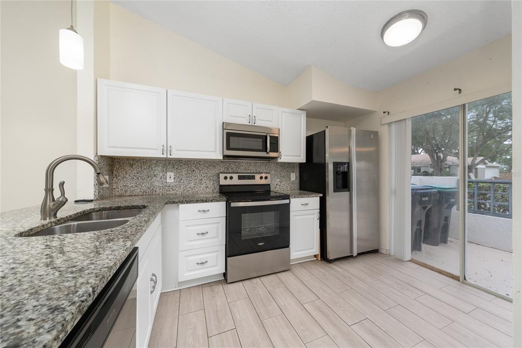 A kitchen features white cabinets, granite countertops, stainless steel appliances, and a sliding glass door — 1262 LUCAYA CIRCLE, ORLANDO, FL