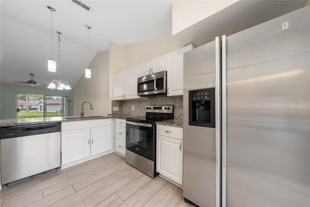 A kitchen features white cabinets, granite countertops, stainless steel appliances, and light wood-look flooring — 1262 LUCAYA CIRCLE, ORLANDO, FL