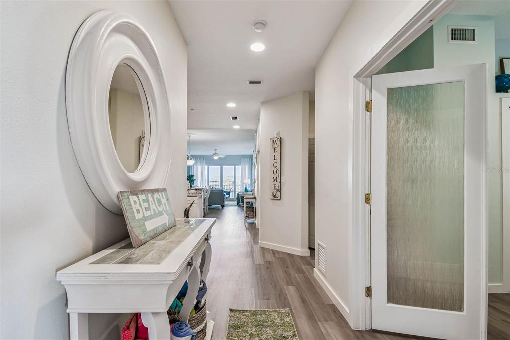 A hallway with a white console table, oval mirror, and view into an open living area — 530 S GULFVIEW BOULEVARD UNIT 304, CLEARWATER BEACH, FL