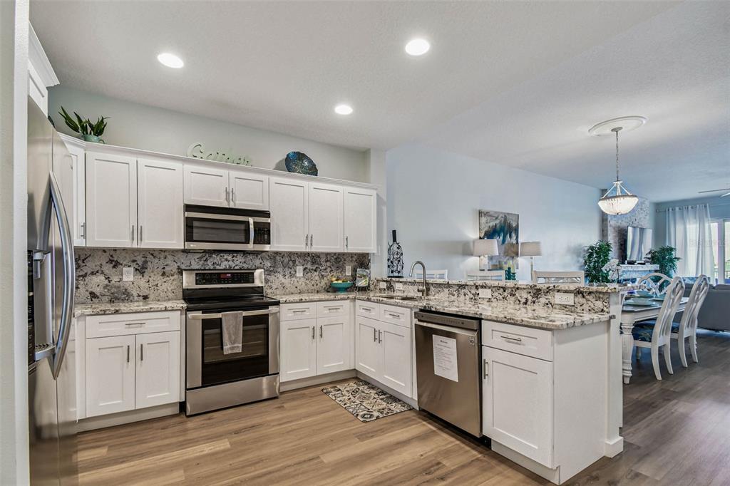 A kitchen with white cabinets, granite countertops, stainless steel appliances, and wood-look flooring — 530 S GULFVIEW BOULEVARD UNIT 304, CLEARWATER BEACH, FL