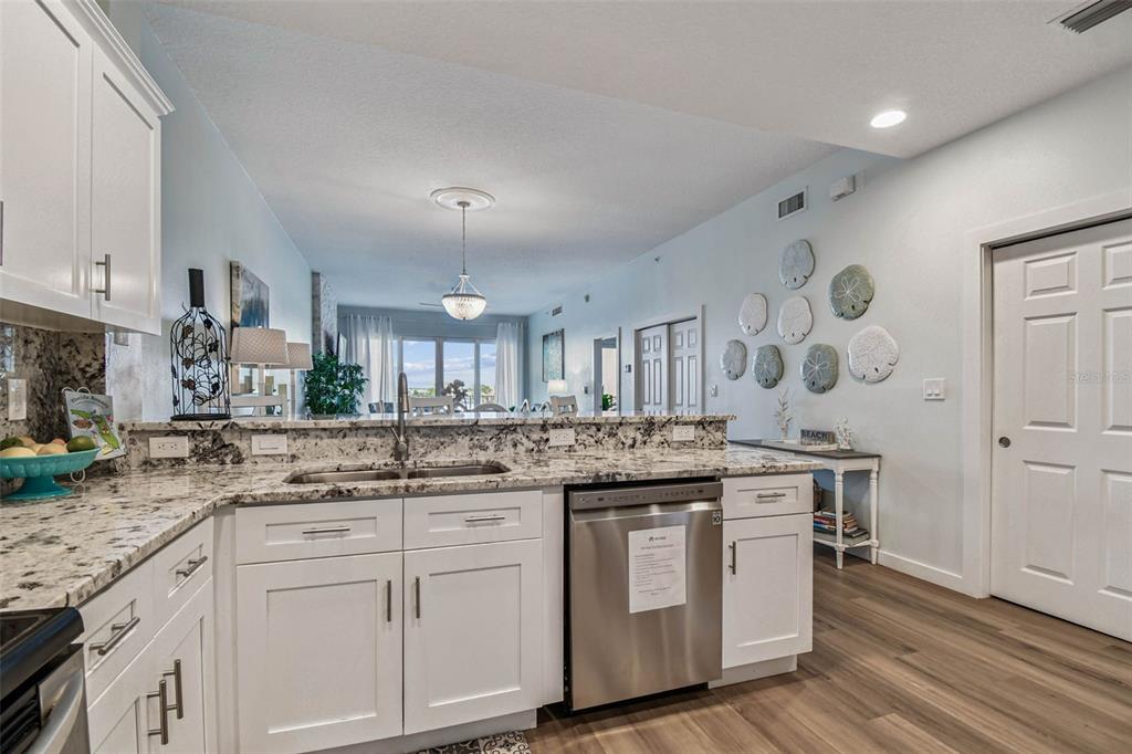 A kitchen with white cabinets, granite countertops, and stainless steel appliances overlooks an open living area — 530 S GULFVIEW BOULEVARD UNIT 304, CLEARWATER BEACH, FL