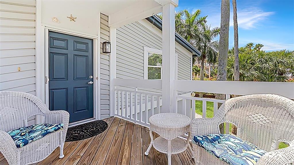 A covered wooden porch features two white wicker chairs, a small table, and a blue door — 1274 SIESTA BAYSIDE DRIVE UNIT 1274-C, SARASOTA, FL