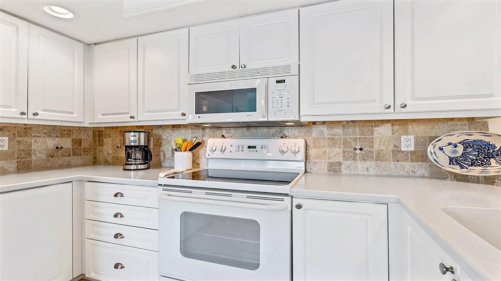 A kitchen features white cabinets, a white stove, a microwave, and a tan tiled backsplash — 1274 SIESTA BAYSIDE DRIVE UNIT 1274-C, SARASOTA, FL
