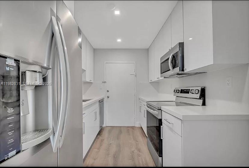 A galley kitchen features white cabinetry, stainless steel appliances, and light wood-look flooring — 5401 Collins Ave # 411, Miami Beach FL 33140, MIAMI BEACH, FL