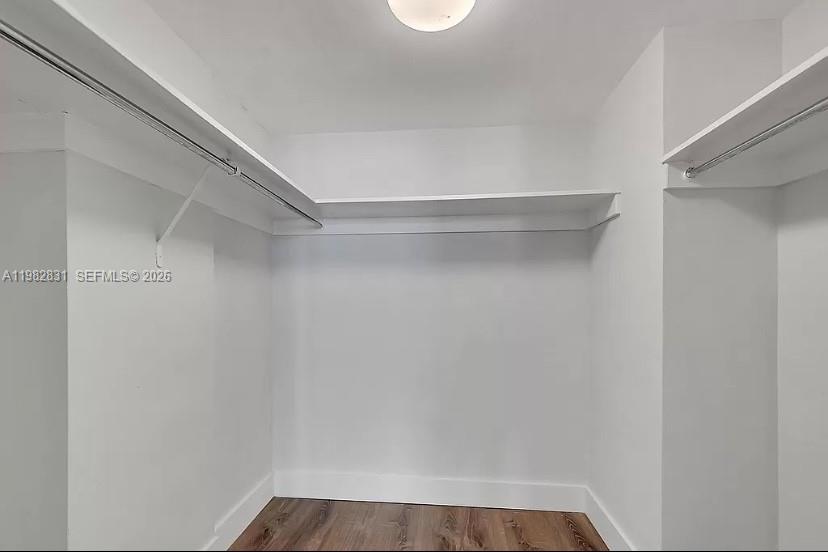 A walk-in closet with white walls, wood-look flooring, and built-in shelving with hanging rods — 5401 Collins Ave # 411, Miami Beach FL 33140, MIAMI BEACH, FL