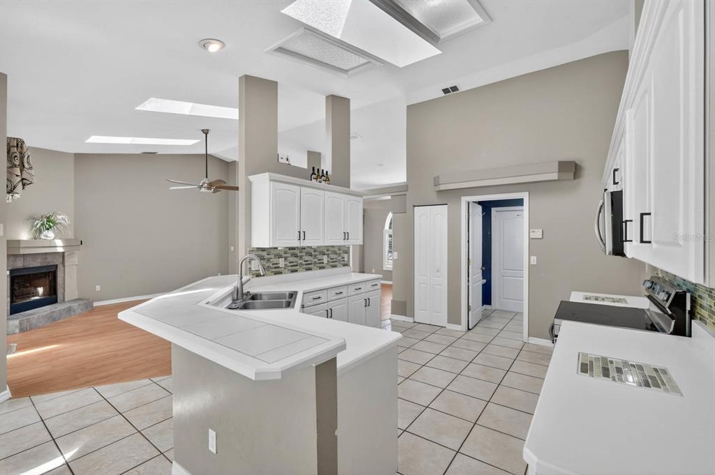 A kitchen with white cabinets, tile countertops, and a breakfast bar overlooking a living area — 5988 SHADY CREEK LANE, PORT ORANGE, FL