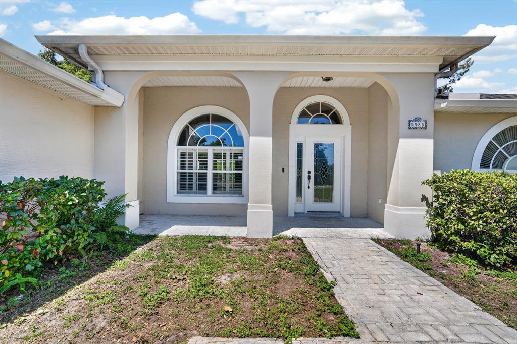 A beige house exterior features a covered entryway with arched windows and a glass door — 5988 SHADY CREEK LANE, PORT ORANGE, FL