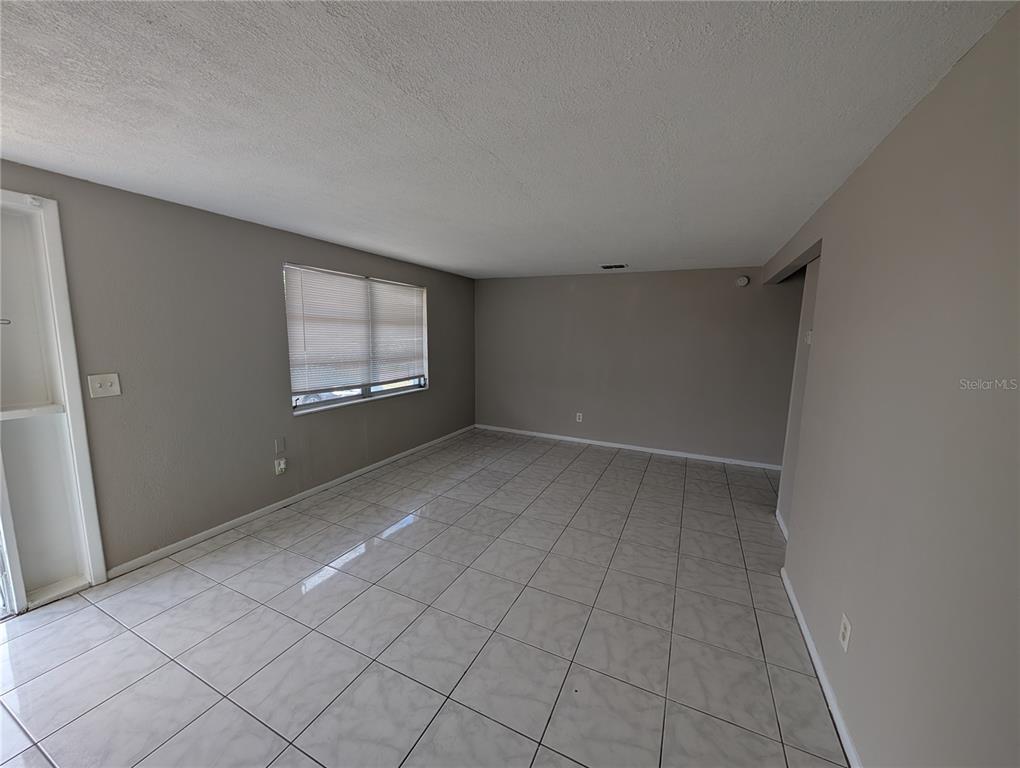 An empty room features light-colored tile flooring, gray walls, and a single window with blinds — 3337 CLYDESDALE DRIVE, HOLIDAY, FL