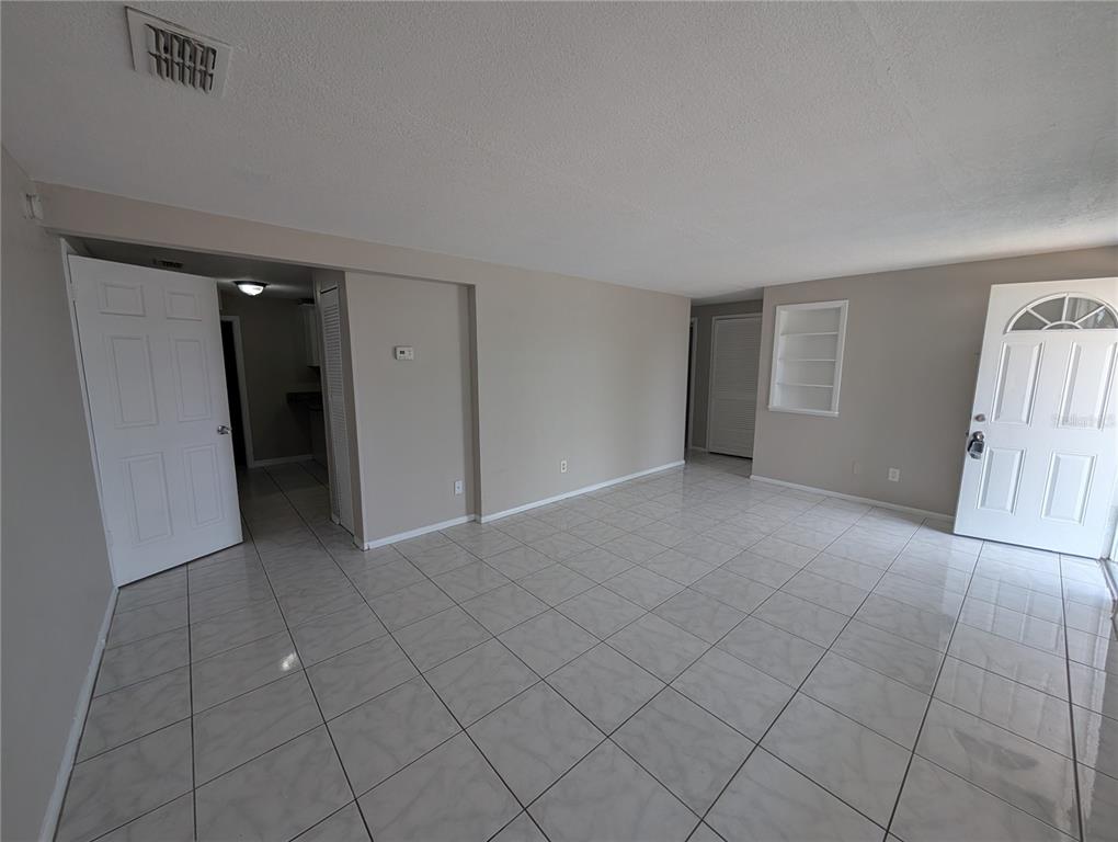 An empty room with light-colored tile flooring, beige walls, and a white front door — 3337 CLYDESDALE DRIVE, HOLIDAY, FL