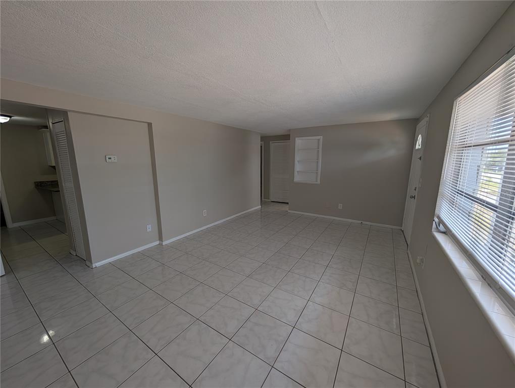 A living room with light-colored tile flooring, beige walls, and a window with blinds — 3337 CLYDESDALE DRIVE, HOLIDAY, FL
