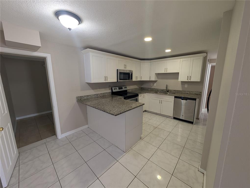 A kitchen features white cabinets, granite countertops, stainless steel appliances, and light-colored tile flooring — 3337 CLYDESDALE DRIVE, HOLIDAY, FL
