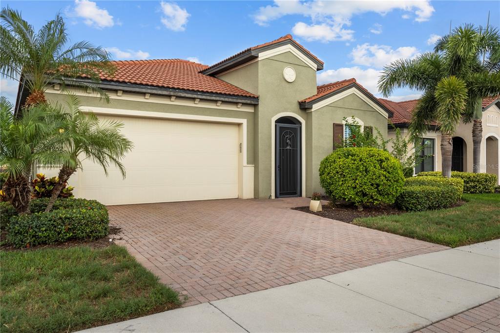 A single-story house with a terracotta tile roof, beige stucco walls, and a paved driveway — 24252 GALLBERRY DRIVE, VENICE, FL