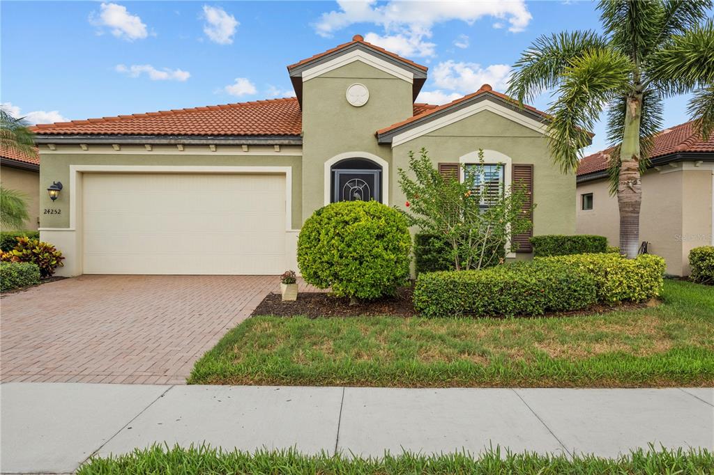 A single-story house with a tan stucco exterior, tile roof, and a two-car garage — 24252 GALLBERRY DRIVE, VENICE, FL