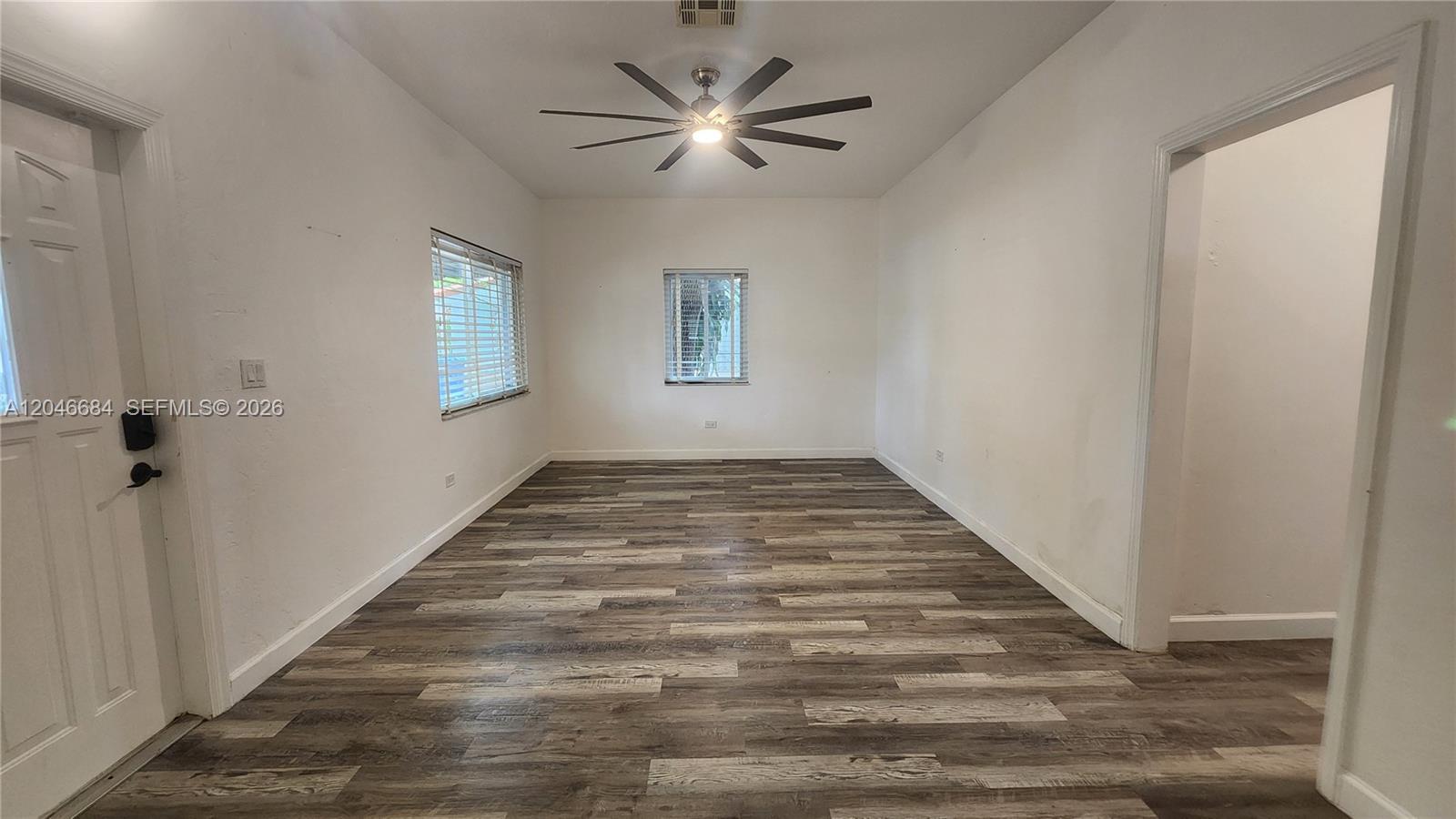 An empty room features white walls, wood-look flooring, two windows, and a ceiling fan — 2174 NE 182nd St, North Miami Beach FL 33162, NORTH MIAMI BEACH, FL