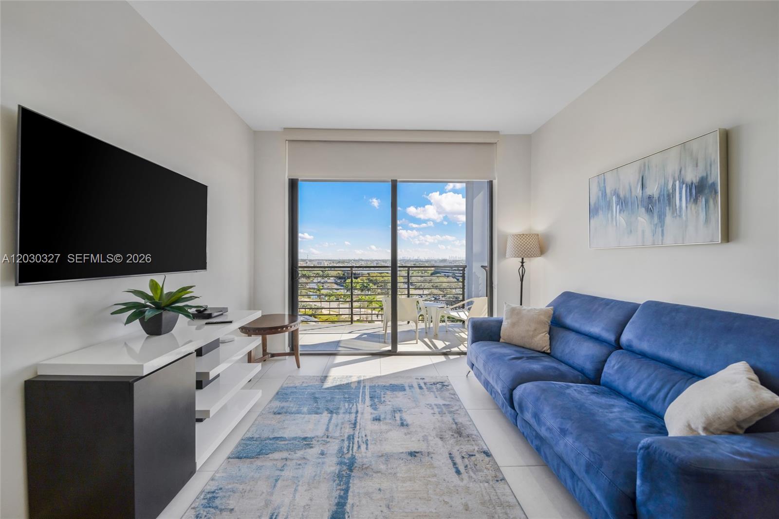 A living room features a blue sofa, a television, and a balcony with outdoor seating — 5350 NW 84th Ave # 903, Doral FL 33166, DORAL, FL