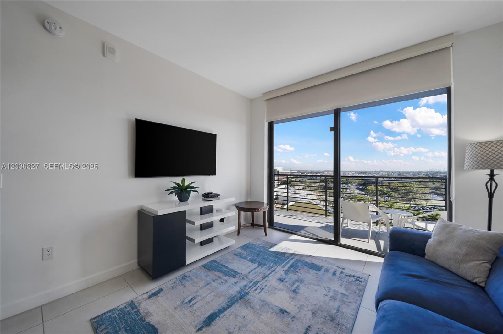 A modern living room features a wall-mounted television, a media console, and a balcony view — 5350 NW 84th Ave # 903, Doral FL 33166, DORAL, FL