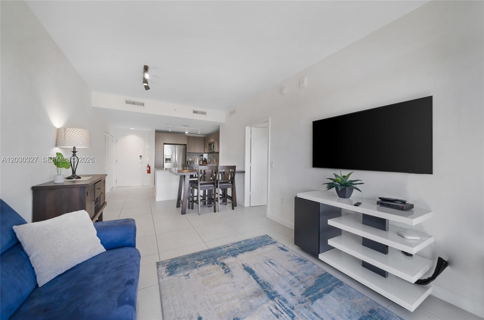 A living room with a blue sofa, a television, and an open kitchen with bar seating — 5350 NW 84th Ave # 903, Doral FL 33166, DORAL, FL