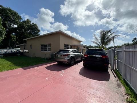 A tan house with a red driveway and two parked cars sits under a cloudy sky — 735 NE 152nd St, Miami FL 33162, MIAMI, FL