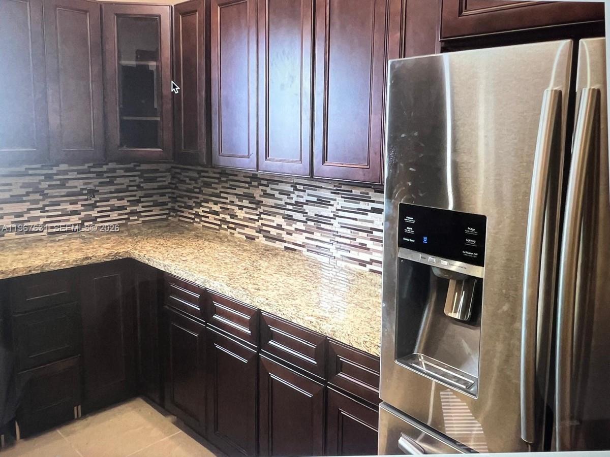 A kitchen features dark wood cabinets, granite countertops, a mosaic tile backsplash, and stainless steel appliances — 735 NE 152nd St, Miami FL 33162, MIAMI, FL