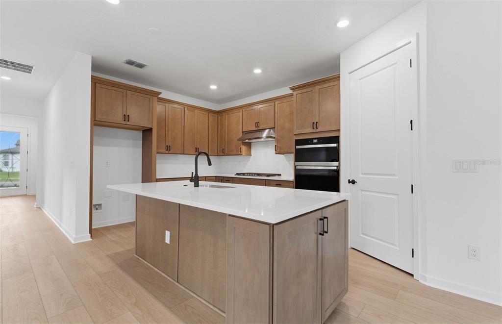 A modern kitchen features light wood cabinets, a white quartz island, and stainless steel appliances — 33456 HERDS HALLOW WAY, WESLEY CHAPEL, FL