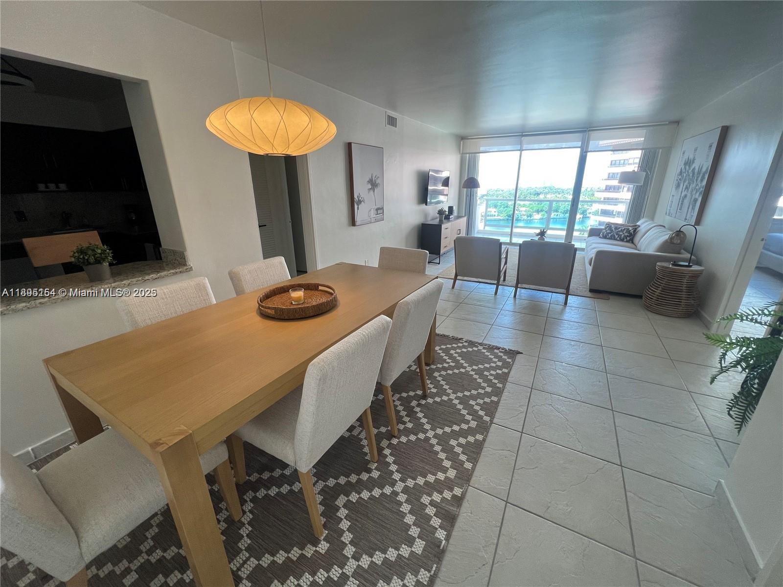 A dining area with a wooden table leads into a living room overlooking the water — 5161 Collins Ave # 1211, Miami Beach FL 33140, MIAMI BEACH, FL