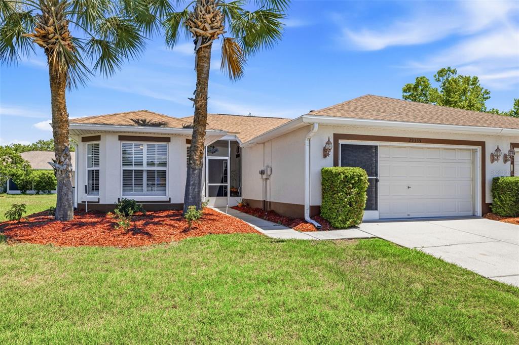 A single-story house with a white stucco exterior, a two-car garage, and two palm trees — 29335 CADDY SHACK LANE E, SAN ANTONIO, FL