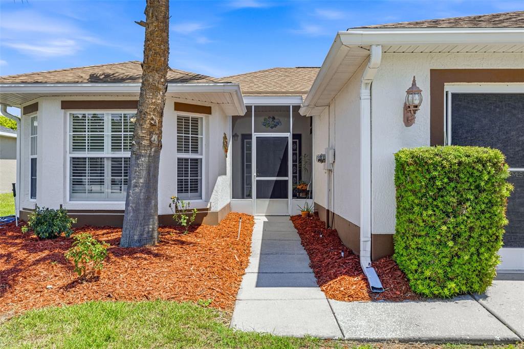 The exterior of a house features a screened entryway, a palm tree, and landscaped mulch beds — 29335 CADDY SHACK LANE E, SAN ANTONIO, FL