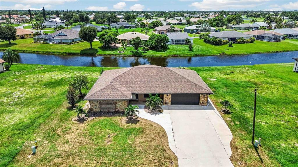An aerial view shows a single-story house with a brown roof, stone accents, and driveway — 166 MARK TWAIN LANE, ROTONDA WEST, FL