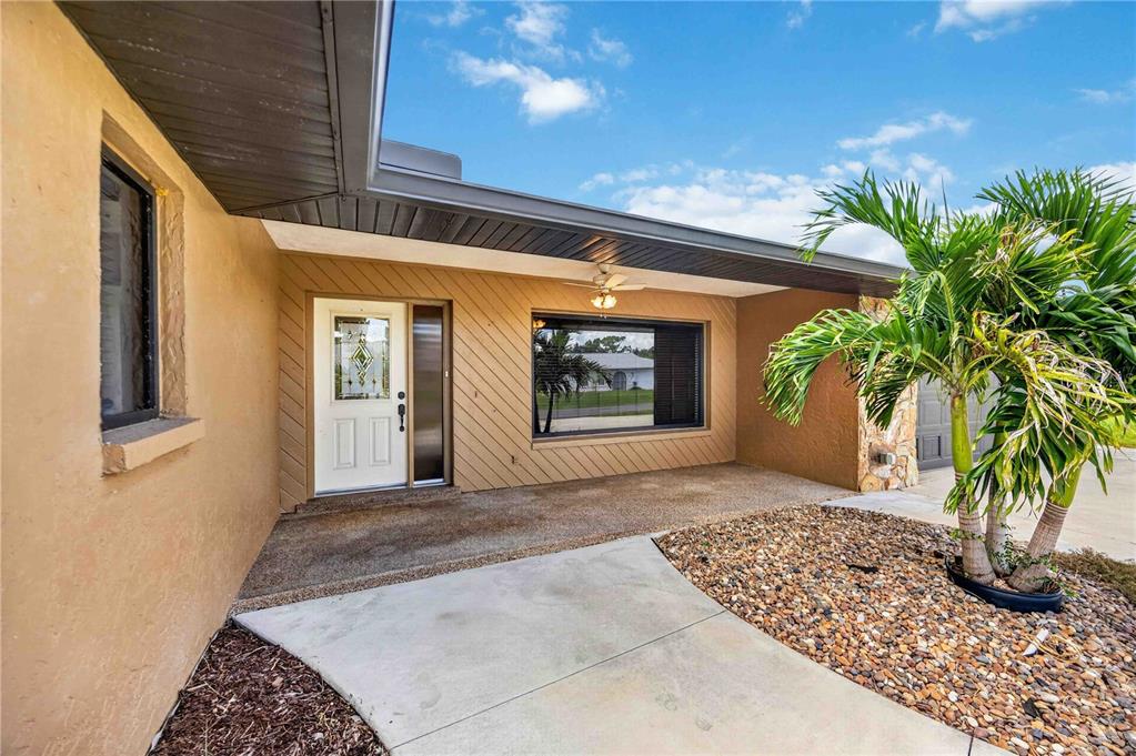 A covered concrete entryway features a white front door, a large window, and a palm tree — 166 MARK TWAIN LANE, ROTONDA WEST, FL