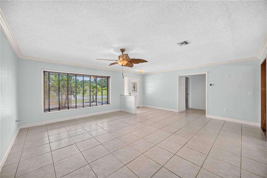 A spacious, light-blue living room features large windows, a ceiling fan, and light-colored tile flooring — 166 MARK TWAIN LANE, ROTONDA WEST, FL