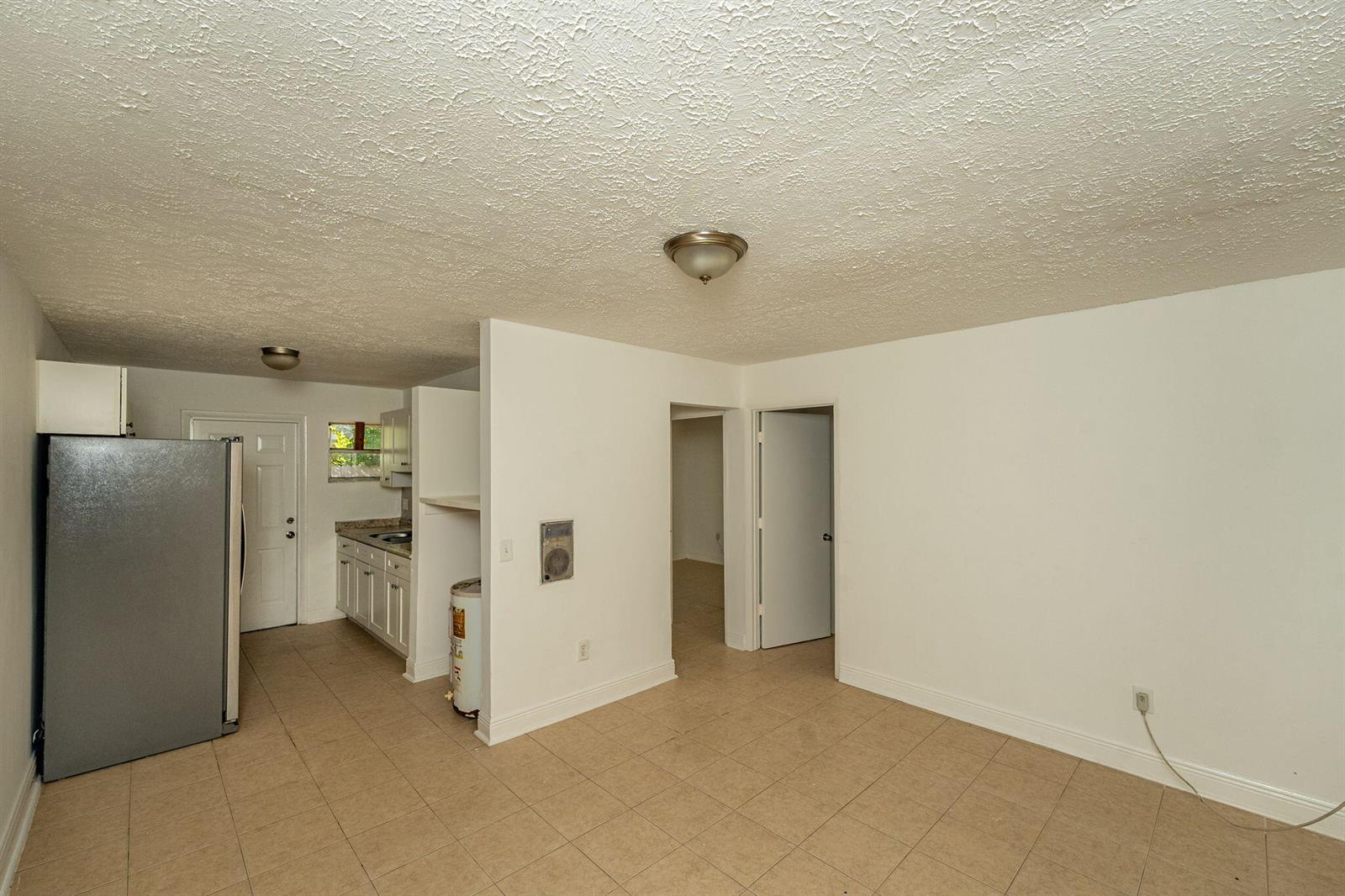 A kitchen and adjacent room with white walls, tile flooring, and a stainless steel refrigerator — 2108 Avenue E, Fort Pierce FL 34950, FORT PIERCE, FL