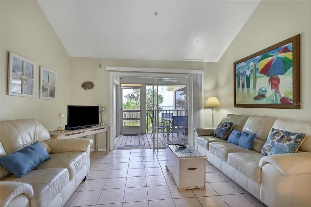 A living room features light tile floors, two cream sofas, and a sliding door to a deck — 9400 LITTLE GASPARILLA ISLAND UNIT E2, PLACIDA, FL
