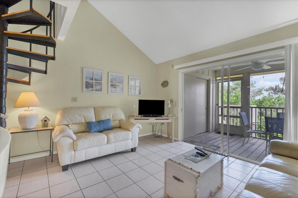 A living room with tile floors, a spiral staircase, and a sliding door to a balcony — 9400 LITTLE GASPARILLA ISLAND UNIT E2, PLACIDA, FL