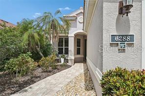 A paved walkway leads to the front entrance of a house with light-colored stucco walls — 6288 WINGSPAN WAY, BRADENTON, FL