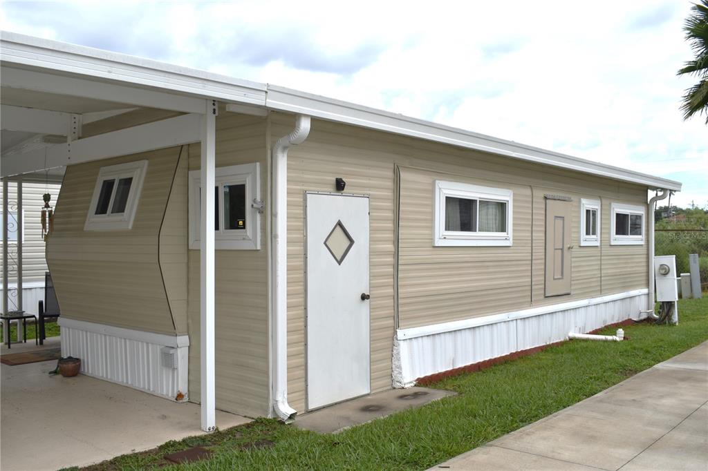 The exterior of a beige mobile home features a white door, windows, and a carport — 9000 US HWY 192 UNIT 52, CLERMONT, FL