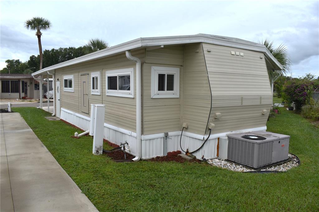 A side view of a beige mobile home with a concrete driveway and air conditioner — 9000 US HWY 192 UNIT 52, CLERMONT, FL