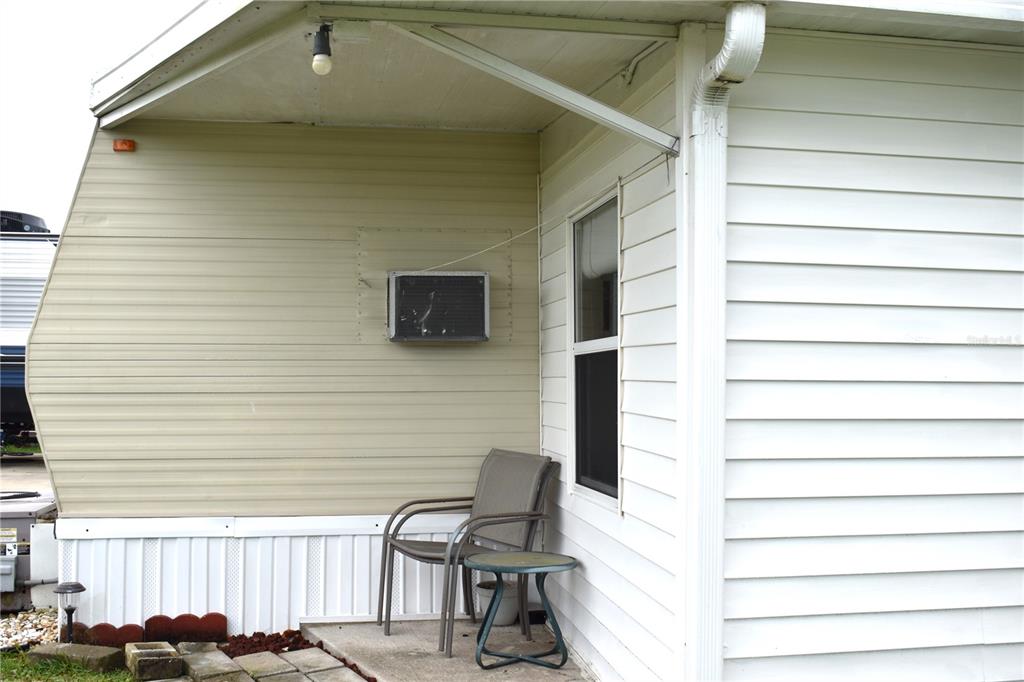 A covered patio area features light-colored siding, a window air conditioning unit, and a chair — 9000 US HWY 192 UNIT 52, CLERMONT, FL