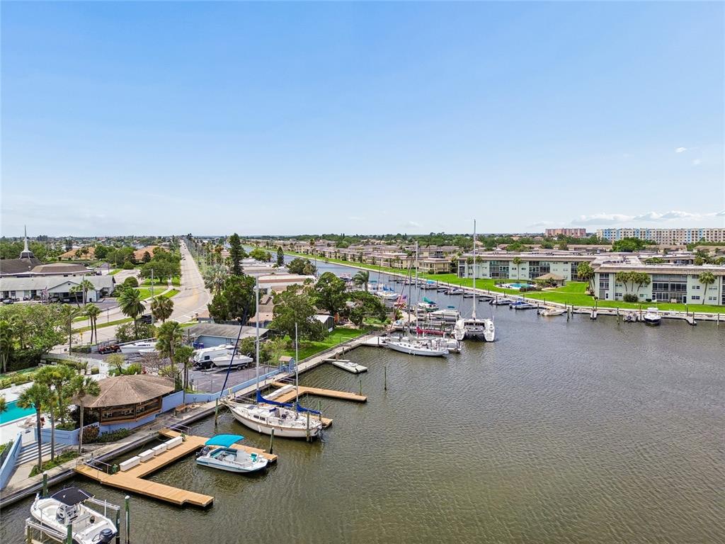 An aerial view shows a canal with docked boats alongside residential buildings and a road — 4939 FLORAMAR TERRACE UNIT 610, NEW PORT RICHEY, FL