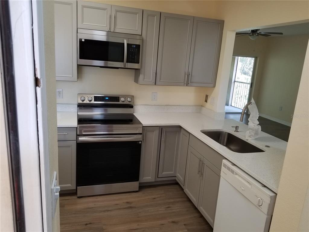 A kitchen features gray cabinets, stainless steel appliances, white countertops, and wood-look flooring — 6022 PORTSDALE PLACE UNIT 202, RIVERVIEW, FL
