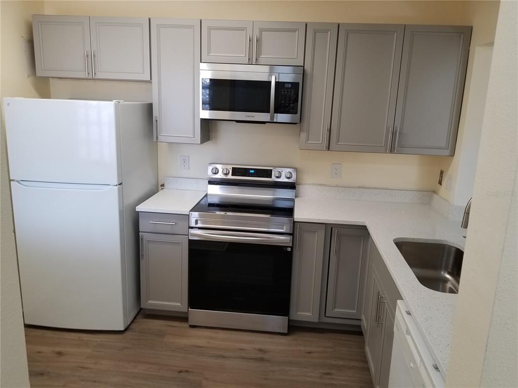 A kitchen features gray cabinets, stainless steel appliances, white countertops, and wood-look flooring — 6022 PORTSDALE PLACE UNIT 202, RIVERVIEW, FL