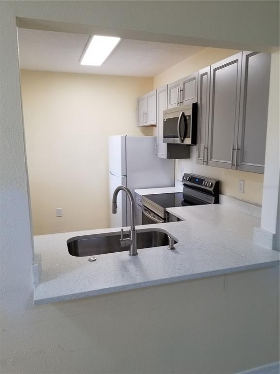 A kitchen features gray cabinets, stainless steel appliances, and a white speckled countertop — 6022 PORTSDALE PLACE UNIT 202, RIVERVIEW, FL