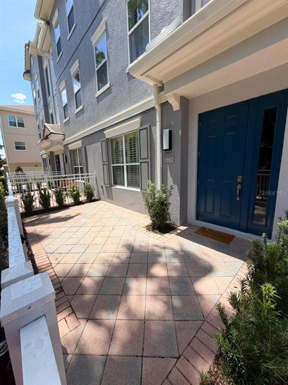 A paved patio leads to a blue front door of a multi-story gray townhouse — 1162 BOLTON PLACE, LAKE MARY, FL