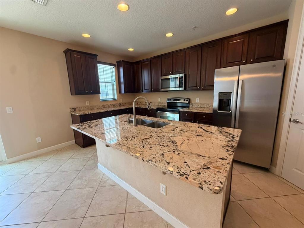 A kitchen features dark wood cabinets, granite countertops, a center island, and stainless steel appliances — 1162 BOLTON PLACE, LAKE MARY, FL
